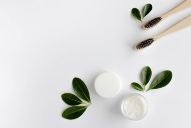 Beyaz arka planda iki ahşap bambu çevre dostu diş fırçası, diş fırçası ve yeşil yapraklar.. 