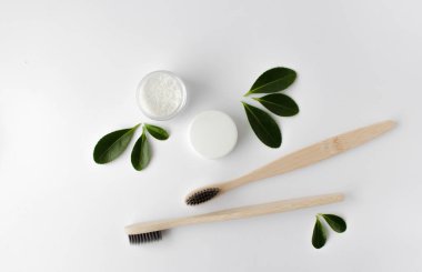 Beyaz arka planda iki ahşap bambu çevre dostu diş fırçası, diş fırçası ve yeşil yapraklar.. 