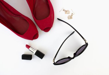 Kırmızı ayakkabılar, kırmızı ruj, güneş gözlüğü ve beyaz arka planda küpeler. Güzellik blogu konsepti. Düz yatıyordu. en üstteki görünüm. 