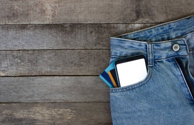 Boş ekranlı Mockup Smartphone ve ahşap arka planda cep kot pantolon kredi kartları. Üst görünüm, metin için yer.