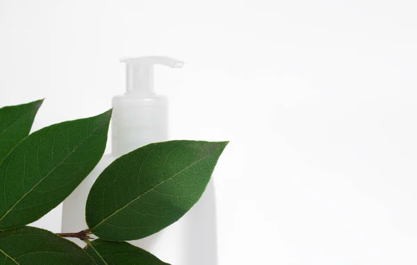 Bílá kosmetická láhev v listí na bílém pozadí — Stock fotografie