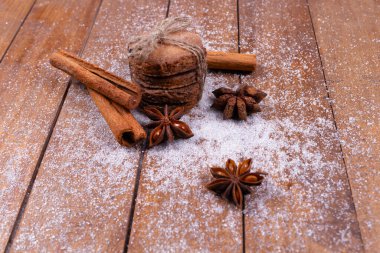 İple bağlanmış bir yığın kurabiye, tarçın çubukları, dekoratif çiçekler beyaz tozun üzerinde, ahşap bir arka planda.