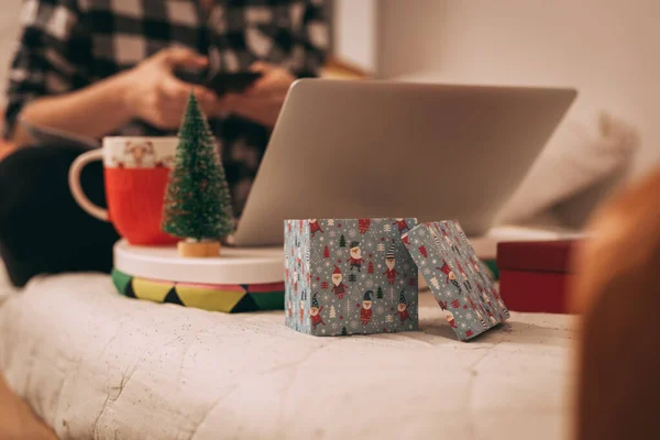 Noel ortamında cep telefonu ve laptop kullanan ekose gömlekli bir kadın.