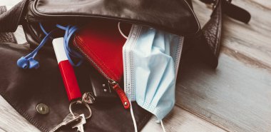 Kadın çantası ahşap zemine düştü ve açıldı, aksesuarlar ve cerrahi maskeyle. Covid-19 konsepti. 