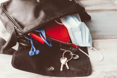 Kadın çantası ahşap zemine düştü ve açıldı, aksesuarlar ve cerrahi maskeyle. Covid-19 konsepti. 