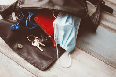 Kadın çantası ahşap zemine düştü ve açıldı, aksesuarlar ve cerrahi maskeyle. Covid-19 konsepti. 