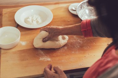 Kadın elleri ev yapımı ekmek hazırlıyor. Mutfakta yaşlı bir kadın hamuru pürüzsüz olana kadar yoğurur.. 