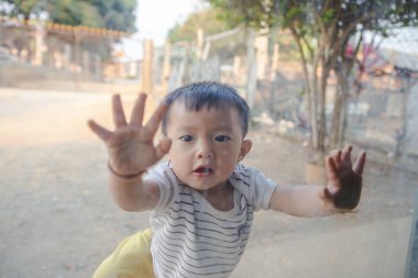 Küçük tatlı Asyalı çocuk aynaya dokun ve gözlüklerle yüzünü kapat.