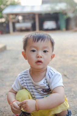 Küçük Asyalı çocuk karada oturup oyuncakçılık ya da kamyonculuk oynuyor.