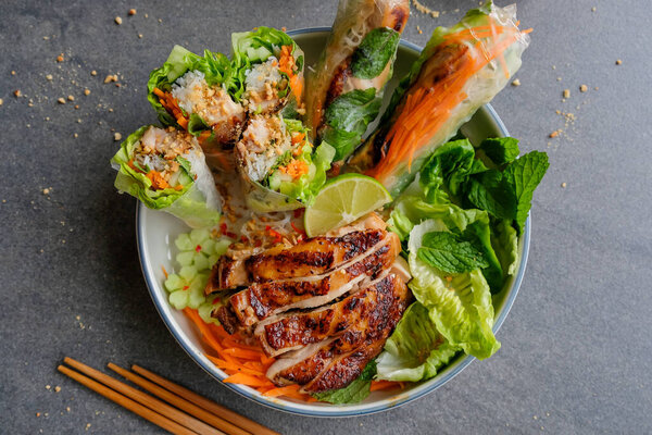 bowl with Vietnamese grilled chicken and spring rolls with chopsticks on table , Healthy and delicious meal, , Homemade Vietnamese cuisine 