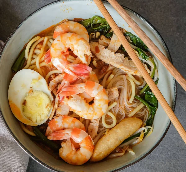 Hokkien Spicy Prawn Noodle Soup of spicy broth with chinese spinach and pork slices with boiled egg and prawns with rice vermicelli in bowl on table, Popular asian local cuisine