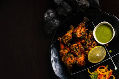  Tabakta kızarmış tavuk, tabakta yeşil sos ve ahşap surfac üzerinde kömür.