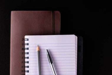 Kahverengi renkli bir günlüğün üzerine kağıt üzerine kalem ve kalem konulmuş açık bir not defterinin yakın çekim görüntüsü - çalışma notları kavramı