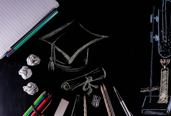 A square academic cap drawn with chalk on blackboard with laboratory experiment diagram and stationary articles scattered on blackboard