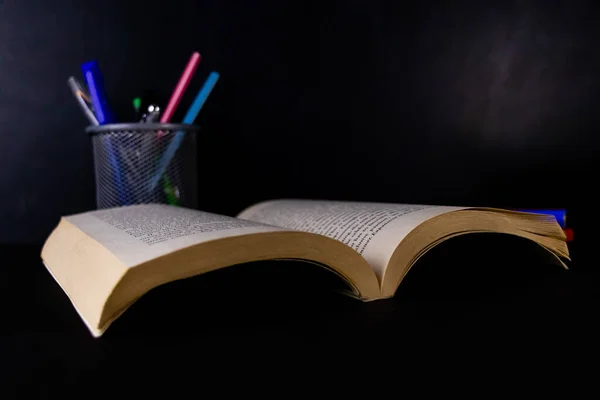 An opened book with a pen stand in the background and blackboard behind -Graduation and classroom concept