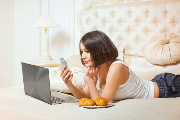 Jonge mooie vrouw liggen op een bed met een laptop — Stockfoto