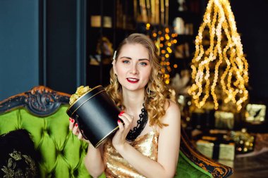 Genç bir kadın, elinde altın süslemelerle bir Noel ağacının arka planında boncuk dizisi tutuyor. Şık kadınlar, şık gece kıyafetleri, aksesuarlar, makyaj. Mutlu yıllar..