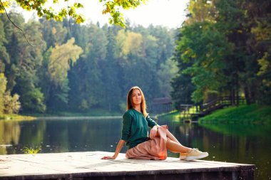 Arka planda nehir ve ormanın rıhtımında oturan rüya gören genç bir kadın..