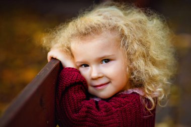 Kıvırcık saçlı küçük sarışın bir kızın büyük portresi. Kameraya bakar ve gülümser..