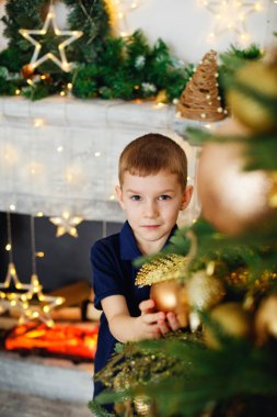 Noel ağacı ve şömine başında çelenk ve hediyelerle süslenmiş sevimli bir çocuk. Yeni yıl havası