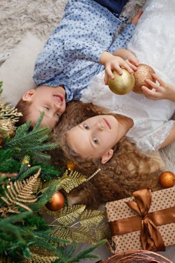 Mutlu küçük kız ve oğlan, erkek ve kız kardeş, halının üzerinde hediyelerle Noel ağacının altında yatıyor. Yukarıdan görünüşü