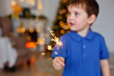 Seçici odaklanma. Bir çocuk Sparkler tutuyor, yakın plan. Maytap ve kıvılcım saçan Makro fotoğraf festivali arka planı, Noel ve yeni yıl için büyülü atmosfer