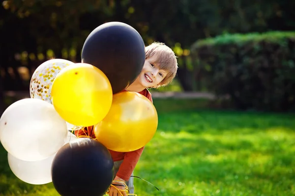 公园里 一个红头发的小男孩在玩一堆黄色的黑色气球 — 图库照片