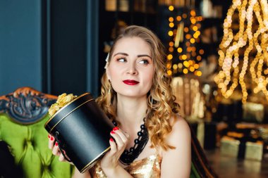 Genç bir kadın, elinde altın süslemelerle bir Noel ağacının arka planında boncuk dizisi tutuyor. Şık kadınlar, şık gece kıyafetleri, aksesuarlar, makyaj. Mutlu yıllar..