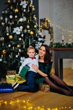 Mutlu bir anne ve Noel 'i kutlayan sevimli bir çocuğun portresi. Yeni yıl tatili. Noel ağacı, süslemeler ve hediyelerle süslenmiş bir odada annesiyle bebek..