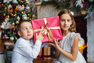 Çocuklar Noel hediyelerini açın. Noel ağacının altında hediye kutularıyla çocuklar. Geleneksel şöminesi olan dekore edilmiş oturma odası. Evde sıcak bir kış günü..