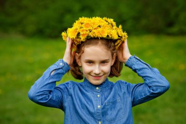 Mavi ceketli bir kız kafasına sarı karahindiba çelengi takıyor. Bahar portresi.
