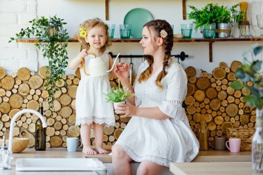 Mutfakta masanın üstünde oynayan küçük bir kız çocuğu, sulama kutusundan çiçekleri suluyor. Anne ve çocuğun mutlu ailesi. Oyunda bir çocuk yetiştirmek.