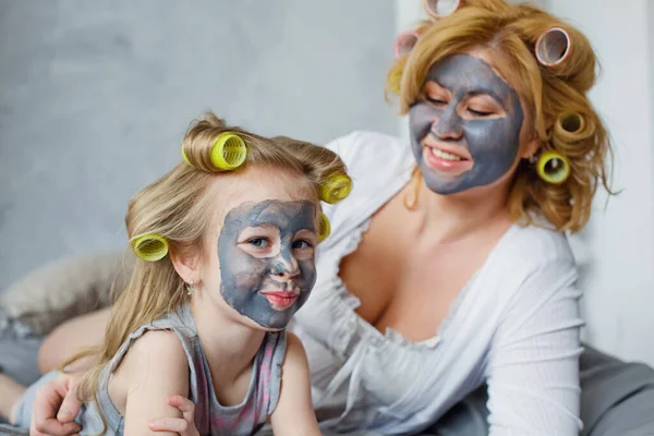 Mother and child do cosmetic procedures together. Happy family mother and baby daughter make a face mask in the bedroom. Concept of a beauty salon, Wellness Spa.