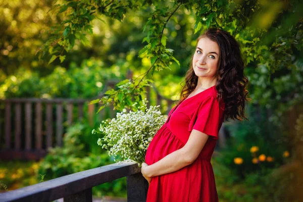 Elinde Çiçekleri Olan Kırmızı Elbiseli Mutlu Hamile Bir Kadın Dinleniyor — Stok fotoğraf