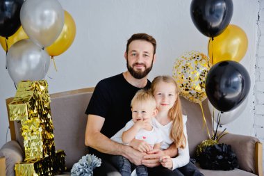 Sevimli çocukları olan mutlu bir babanın portresi. Bir tatil evinde aile fotoğrafı için poz veriyor. Kameraya bakarken küçük tatlı bir kız ve oğlana sarılıyor.