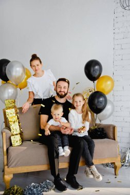 Kanepede oturan sevimli çocukları olan bir anne ve babanın bir tatil evindeki aile fotoğrafı için poz verişi. Küçük tatlı oğlana ve kızına sarıl, konfeti at.