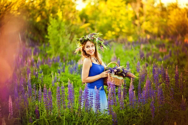 頭に花の花輪を持つ女の子は 紫色のラインのあるフィールドで日没時に花のバスケットで立っています 選択的焦点 トーニング およびノイズ効果を持つ画像 — ストック写真