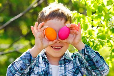 Bahçede eğlenen bir çocuğun portresi gözlerine tutulmuş Paskalya yumurtalarıyla yeşilliğin arka planına karşı..