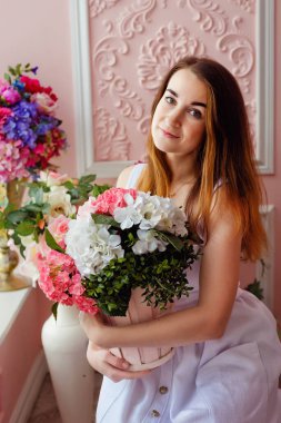 Pembe odada bir buket çiçekle beyaz, zarif elbiseli esmer bir kadın.