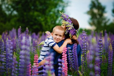 Bir anne oğlunu kollarına alır çiçek açan leylak çiçekleri tarlasında.