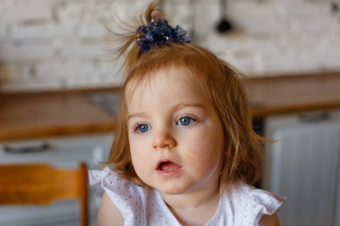 Küçük bir kız mutfak masasında oturuyor. Rahat, gerçek bir hayat ortamında..