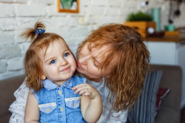 Sevgi dolu bir anne çocuğuyla oynar. Anne ve kızı ahşap zeminde büyük bir pencerenin yanında oturuyorlar..