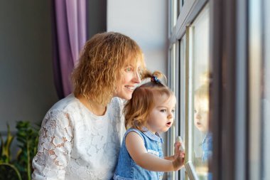 Sevgi dolu bir anne çocuğuyla oynar. Bir anne kızını büyük bir pencerenin yanında kollarına alır..