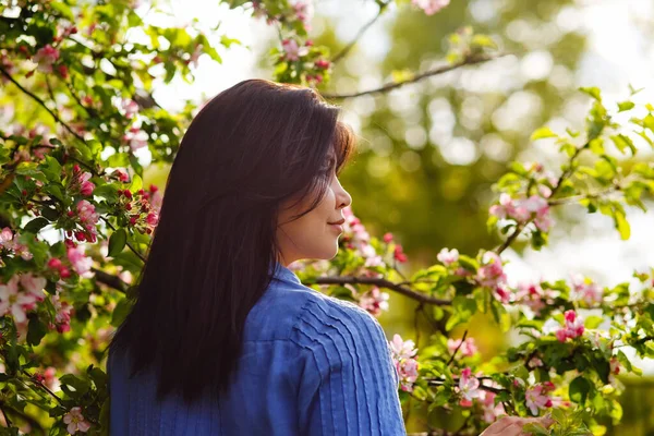Genç ve çekici bir kadın, koyu renk saçlı, mavi elbiseli, bahar çiçekli bir bahçede poz veriyor. Bahar geldi..