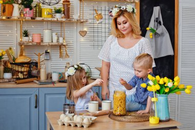 Anne ve çocuklar mutfakta makarna ile oturuyorlar. Bir erkek ve bir kız annelerine yemek hazırlamalarında yardım ederler..