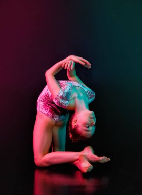 Denge. Bir kız genç bir sporcu, neon rengi açık renkli siyah bir arka planda izole bir şekilde poz veren bir jimnastikçi..