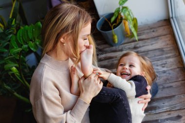 Sevgi dolu bir anne kucağında sevimli bir çocuk taşır ve kızı evde oynar. Pencere kenarındaki pencerede birlikte eğleniyorlar..