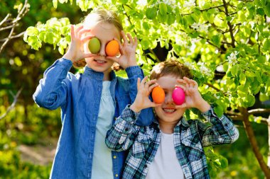 Çocuklar bahar bahçesinde Paskalya yumurtası avında. Küçük çocuk ve anaokulu kızı açık havada oynuyorlar. Taşaklarını gözlerinin önüne koyuyorlar..