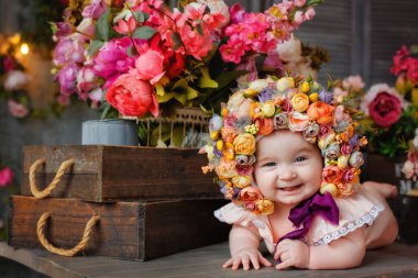 Çiçeklerden yapılmış bir şapkayla altı aylık güzel bir kız bebek, pencerenin yanında karnının üstünde yatıyor. Başında çelenkle çiçeklerin arasında küçük bir çocuk..