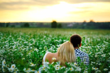 Genç bir çift gün batımında papatya tarlasında kucaklaşır. Kameraya dön. Gün batımını izliyorlar..